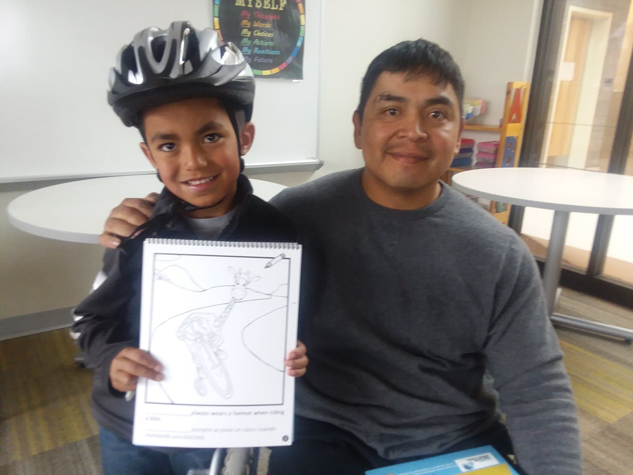 A happy Navajo student with his new helmet and bicycle safety book donated by the NM Brain Injury Awareness Council accompanied by Josh Longhat, ThinkFirst Navajo VIP.