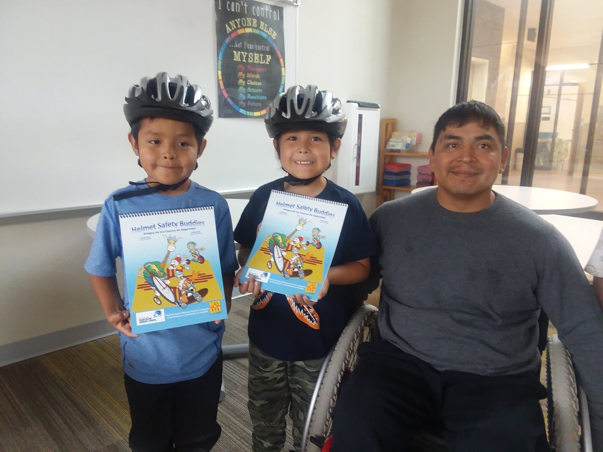 Two smiling Lincoln Elementary School students with their new helmets and guidebooks on bicycle safety with ThinkFirst Navajo VIP, Josh Longhat.